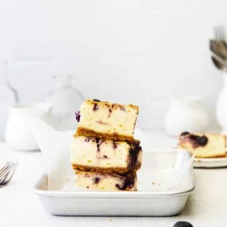 3 Gluten Free Blueberry Cheesecake Bars stacked on a 1/8 sheet pan lined with white parchment paper