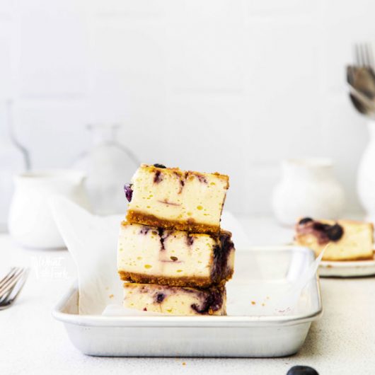 3 Gluten Free Blueberry Cheesecake Bars stacked on a 1/8 sheet pan lined with white parchment paper