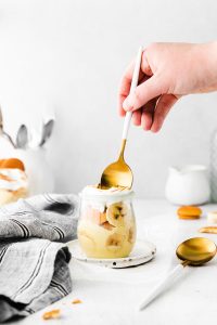 a spoonful of banana pudding being scooped out of a small glass jar with a gold and white spoon