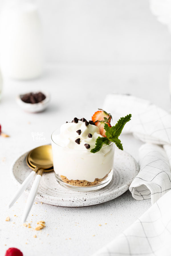 cheesecake mousse in a small glass bowl garnished with graham cracker crumbs, chocolate chips, strawberries, and mint