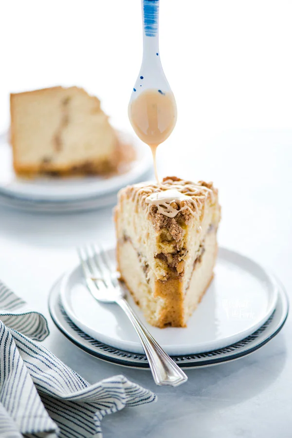 maple glaze being drizzled on a slice of gluten free sour cream coffee cake