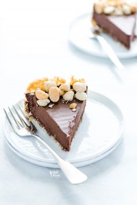 a slice of Macadamia Nut Chocolate Pie with Coconut Crust on a stack of 2 white plates with a silver fork