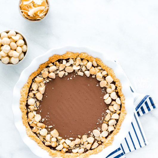 overhead shot of a Macadamia Nut Chocolate Pie with Coconut Crust on a blue and white striped cloth napkin