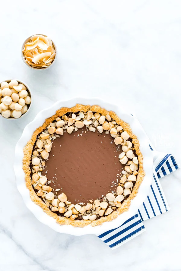 overhead shot of a Macadamia Nut Chocolate Pie with Coconut Crust on a blue and white striped cloth napkin