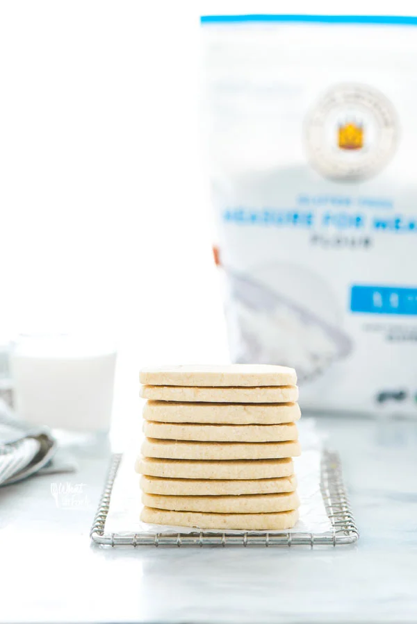 a stack of Gluten Free Shortbread Cookies on a small metal wire rack lined with wax paper with a bag of King Arthur Gluten Free Measure for Measure Flour in the background