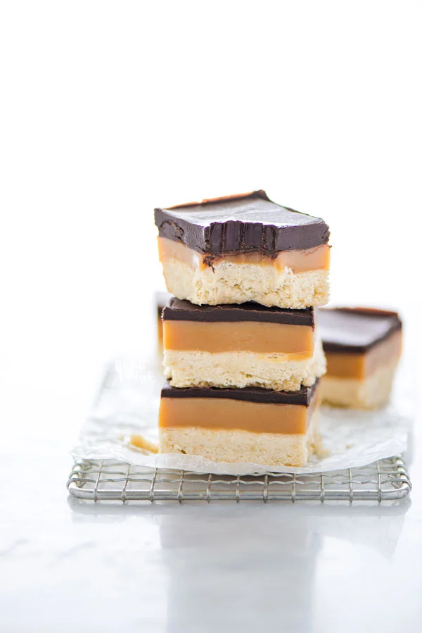 a stack of Gluten Free Millionaire Shortbread bars on a wire rack with a bite taken out of the top bar