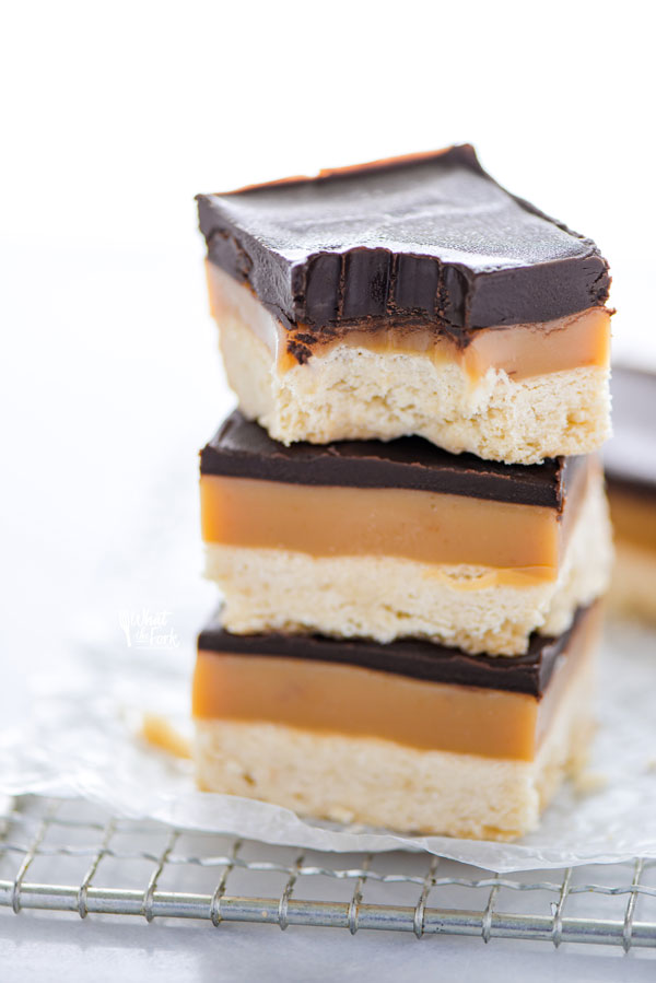 close up shot of a stack of 3 Gluten Free Millionaire Shortbread bars on a wire rack with the top one with a bite taken out