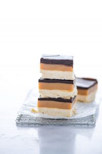 a stack of 3 Gluten Free Millionaire Shortbread Bars on a small wire rack lined with wax paper