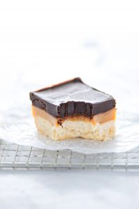 a Gluten Free Millionaire Shortbread bar on a wax paper lined wire rack with a bite taken out