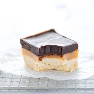 a Gluten Free Millionaire Shortbread bar on a wax paper lined wire rack with a bite taken out