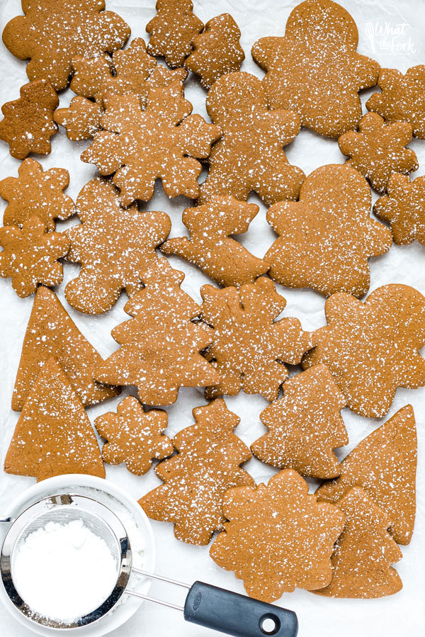 overhead shot of gluten free gingerbread cookies on a parchment paper lined baking sheet dusted with parchment paper
