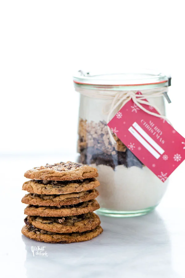 a stack of gluten free chocolate toffee cookies in front of a gluten free christmas cookie jar