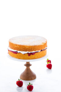 a gluten free Victoria Sponge Cake on a wood and marble cake stand - 2 layers of vanilla sponge cake layered with strawberry jam and whipped cream
