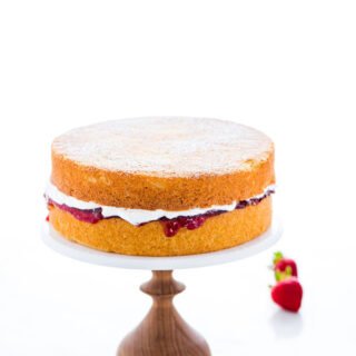 a gluten free Victoria Sponge Cake on a wood and marble cake stand - 2 layers of vanilla sponge cake layered with strawberry jam and whipped cream