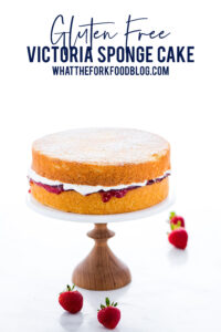 gluten free Victoria Sponge Cake on a marble cake stand with a wood base. Image includes text for Pinterest
