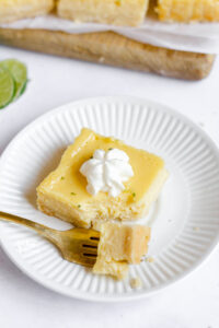 a gluten free key lime pie bar on a small round white plate with a bite-sized piece on a gold fork