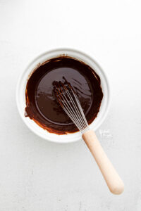 overhead shot of chocolate ganache in a white bowl with a wood handled whisk