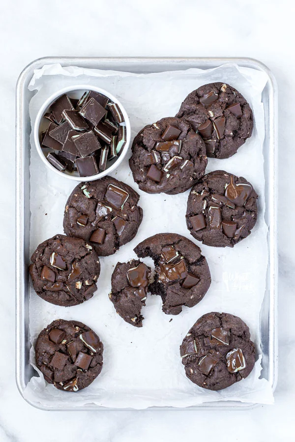 overhead shot of Gluten Free Andes Mint Chocolate Chip Cookies on a parchment paper lined quarter sheet pan with one broken in half