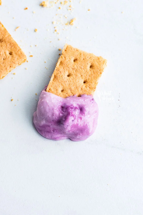 blueberry cheesecake dip on a piece of graham cracker on a white surface
