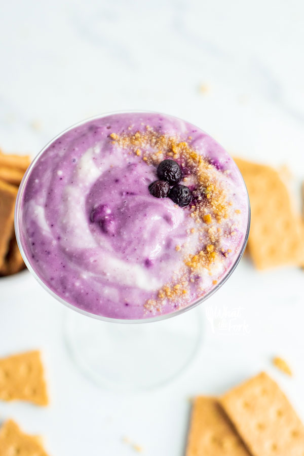 blueberry cheesecake dip in a vintage martini glass garnished with crushed graham cracker crumbs and frozen blueberries