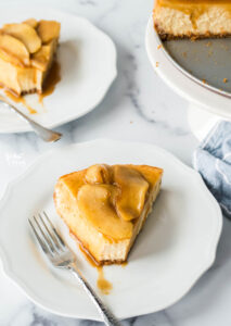 2 pieces of gluten free caramel apple cheesecake on white plates with silver forks