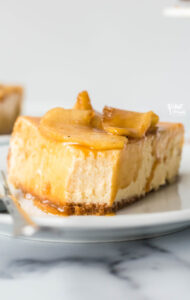 a slice of gluten free caramel apple cheesecake on a white plate with a silver fork that has a bite taken out