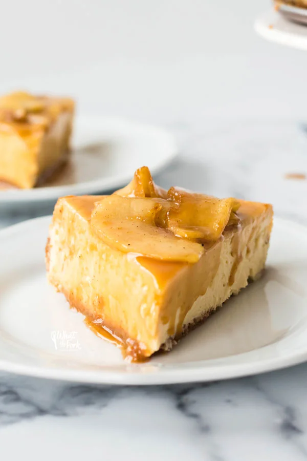 a slice of gluten free caramel apple cheesecake on a white plate with a second piece on a white plate in the back left corner