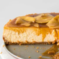 straight on shot of a gluten free caramel apple cheesecake that's been cut into with caramel dripping down the side