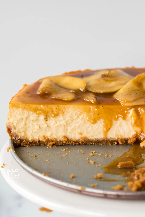 straight on shot of a gluten free caramel apple cheesecake that's been cut into with caramel dripping down the side