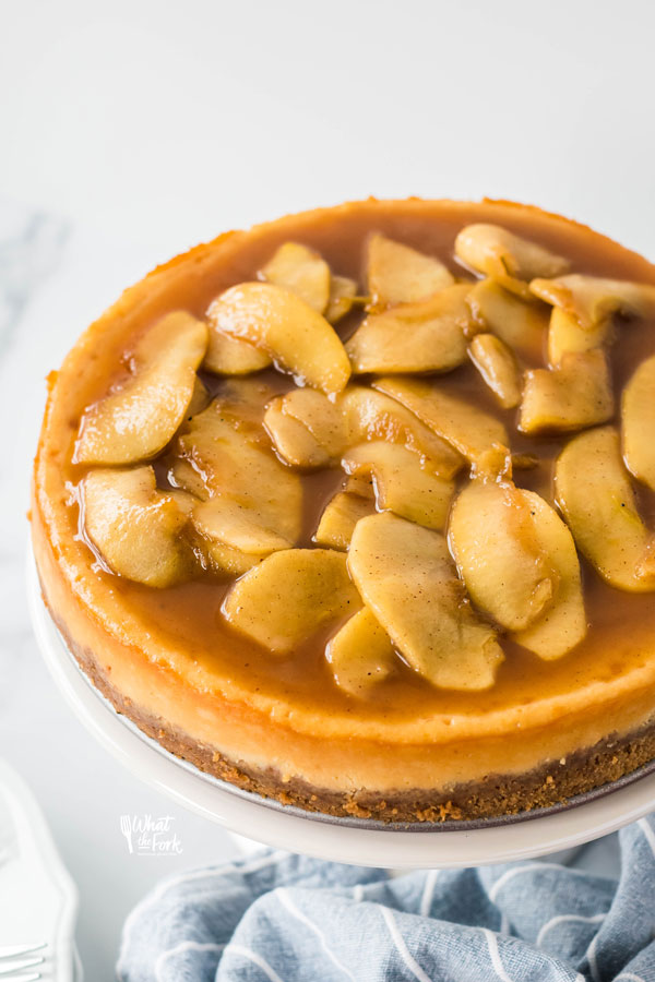 a Gluten Free Caramel Apple Cheesecake on a white cake stand ready to be served