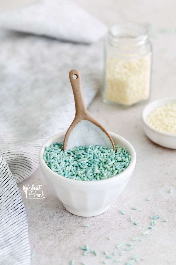 blue sprinkles in a small white bowl with a brown rimmed white spoon in it