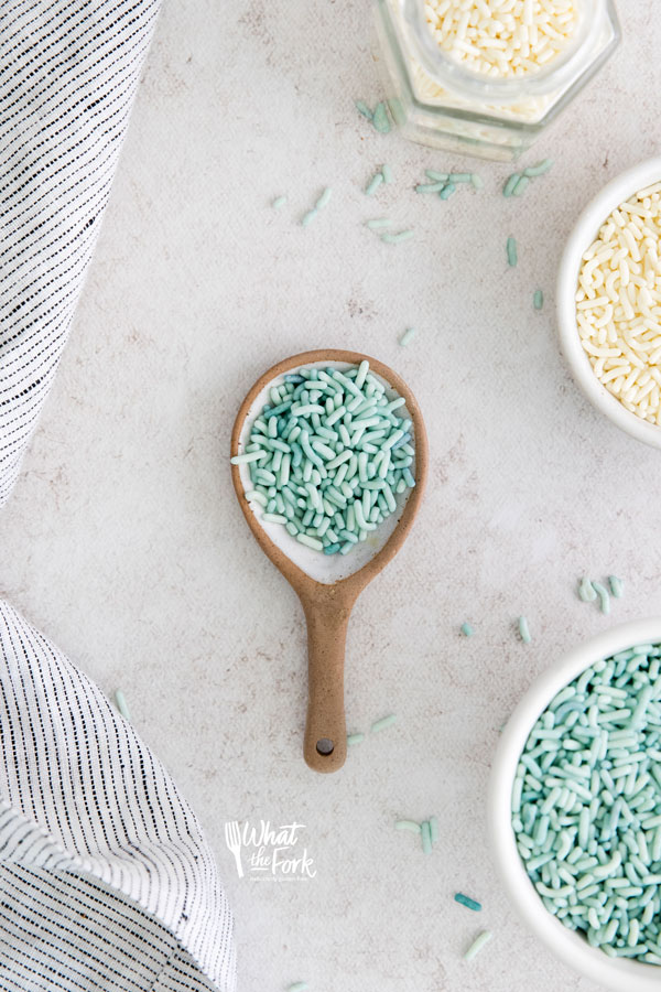 overhead shot of blue sprinkles in a white and brown pottery spoon