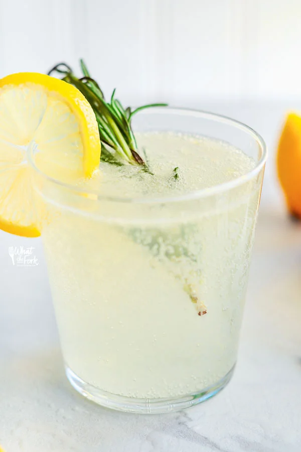 Non-Alcoholic Rosemary Citrus Spritzers in a clear glass garnished with a wheel of lemon and sprig of fresh rosemary