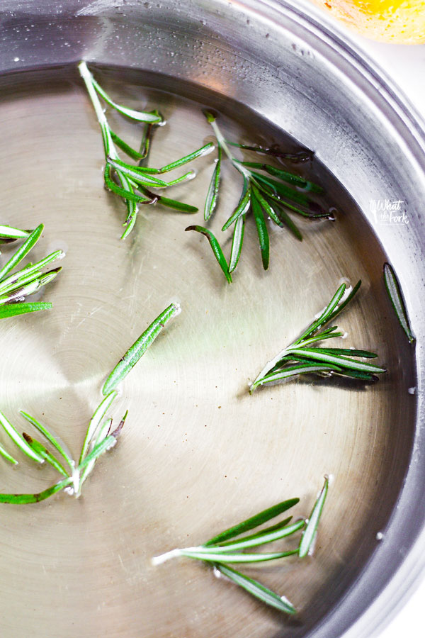 How to Make Simple Syrup with Rosemary - simple syrup with sprigs of rosemary in it in a metal pan