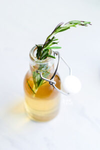 a bottle of Rosemary Simple Syrup with a sprig of rosemary in the top