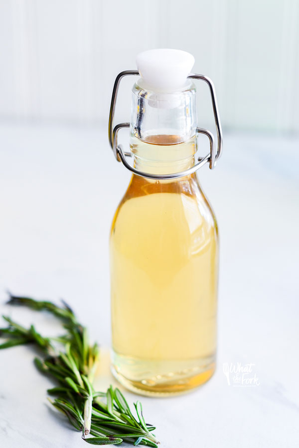 learn how to make simple syrup with rosemary! This image shows a bottle of rosemary simple syrup with a sprig of rosemary next to it.