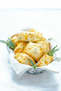 baked Gluten Free Cheddar Sage Biscuit Recipe with the biscuits in a wire bread basket lined with a white flour sack towel garnished with fresh sage sprigs