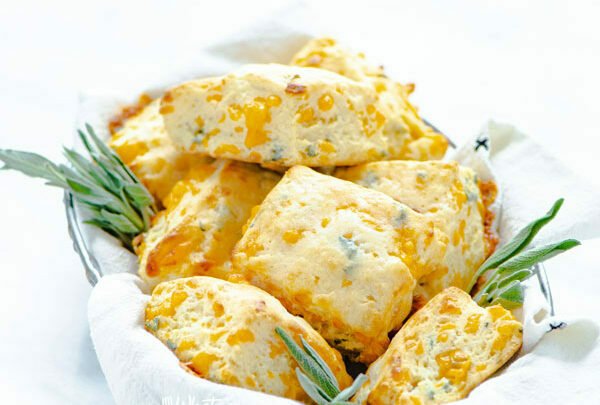 baked Gluten Free Cheddar Sage Biscuit Recipe with the biscuits in a wire bread basket lined with a white flour sack towel garnished with fresh sage sprigs