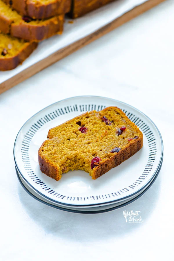 a slice of Gluten Free Pumpkin Cranberry Bread with a bite taken out on a white plate with black stripes