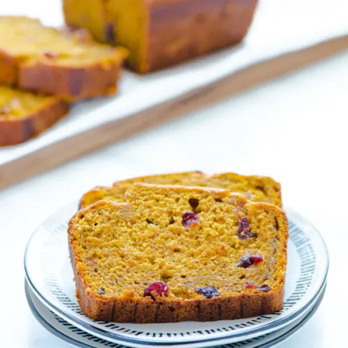 2 slices of Gluten Free Pumpkin Cranberry Bread on a stack of white and black plates