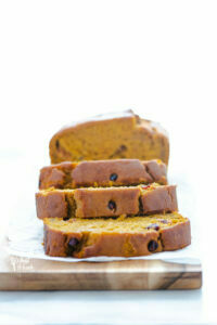 straight on shot of sliced Gluten Free Pumpkin Cranberry Bread on a rectangle wood cutting board lined with wax paper