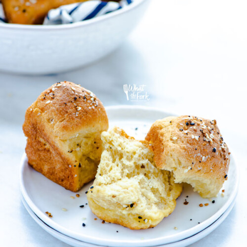 baked Gluten Free Rolls Recipe with Everything Bagel Seasoning with 2 rolls on a stack of 2 small white plates. one rolls is whole while the other is ripped in half to show the middle