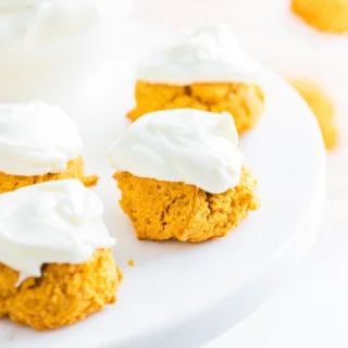 gluten free pumpkin cookies on a white cake stand frosted with cream cheese frosting