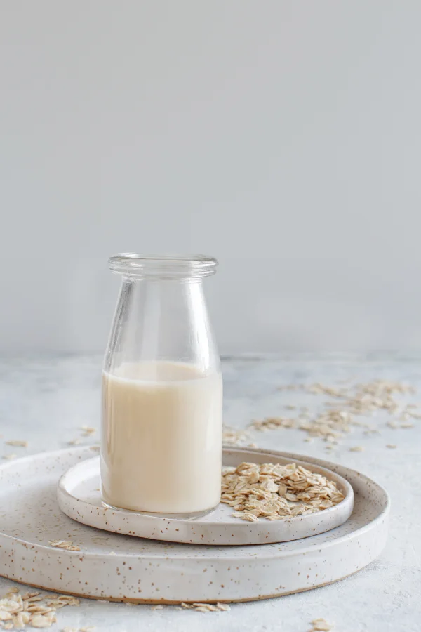 oat milk in a small jug on a white plate with oats