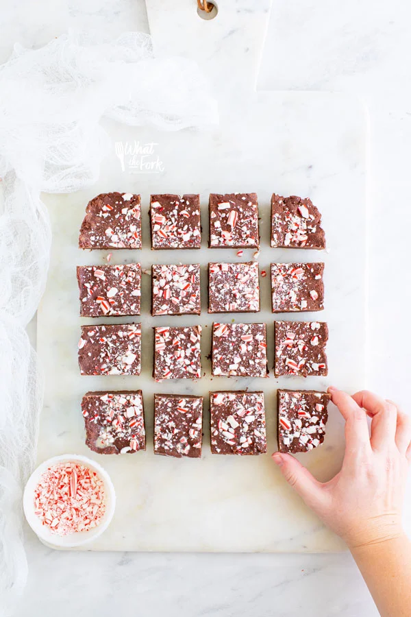 overhead shot of an easy peppermint fudge recipe cut on a white surface with a hand taking a piece