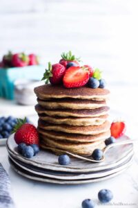 straight on shot of a stack of gluten free sourdough pancakes on a white plate topped with fresh strawberries and blueberries