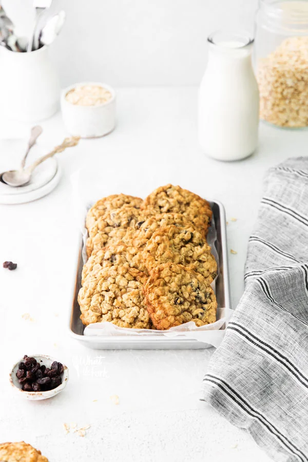 gluten free oatmeal raisin cookies piled on a small silver metal sheet pan lined with white parchment paper