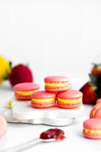 Pink Strawberry Lemon Macarons filled with yellow lemon buttercream are stacked on a small white marble board