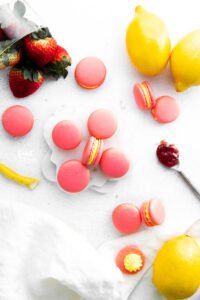 overhead shot of pink Strawberry Lemon Macarons on a white surface with whole lemons and strawberries