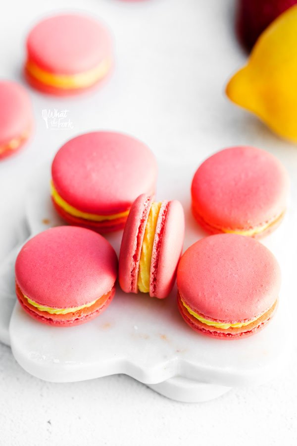 Pink Strawberry Lemon Macarons on a small white marble board are filled with yellow lemon buttercream
